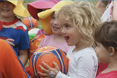 children outside smiling and holding soccer balls